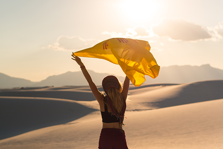 Female in sand dunes with NM flag