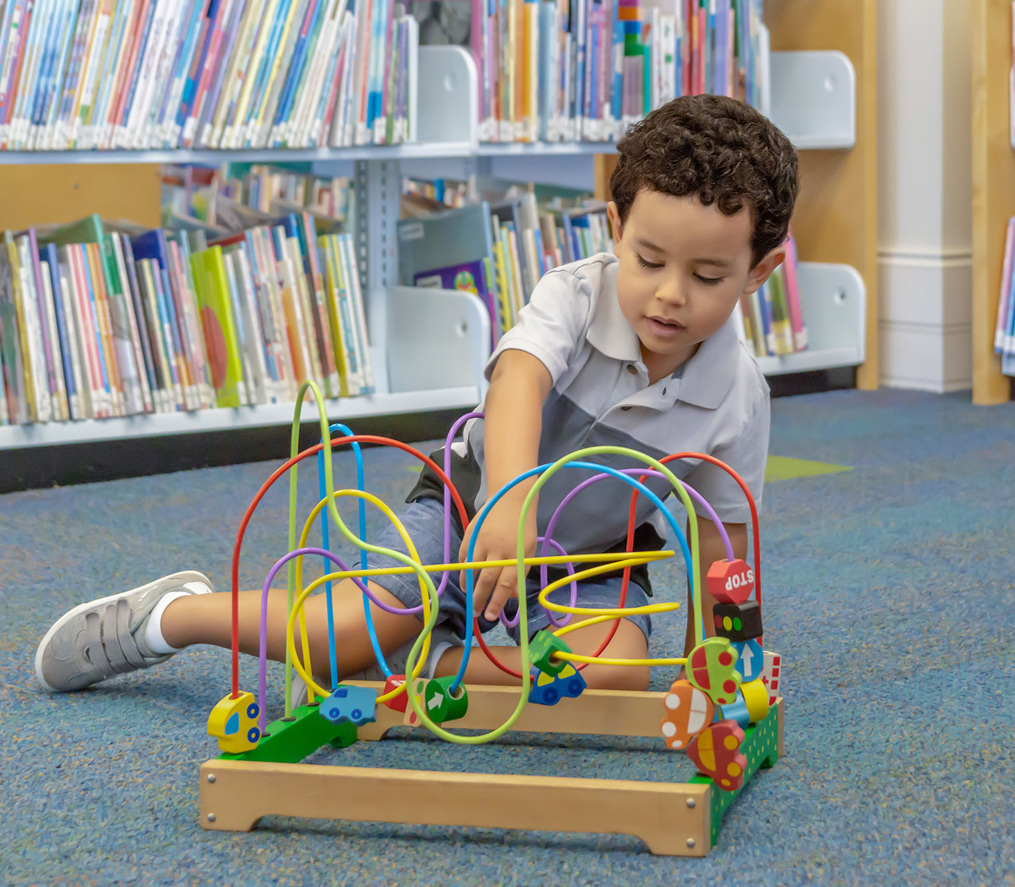 boy playing on the floor of a library with a wire maze puzzle
