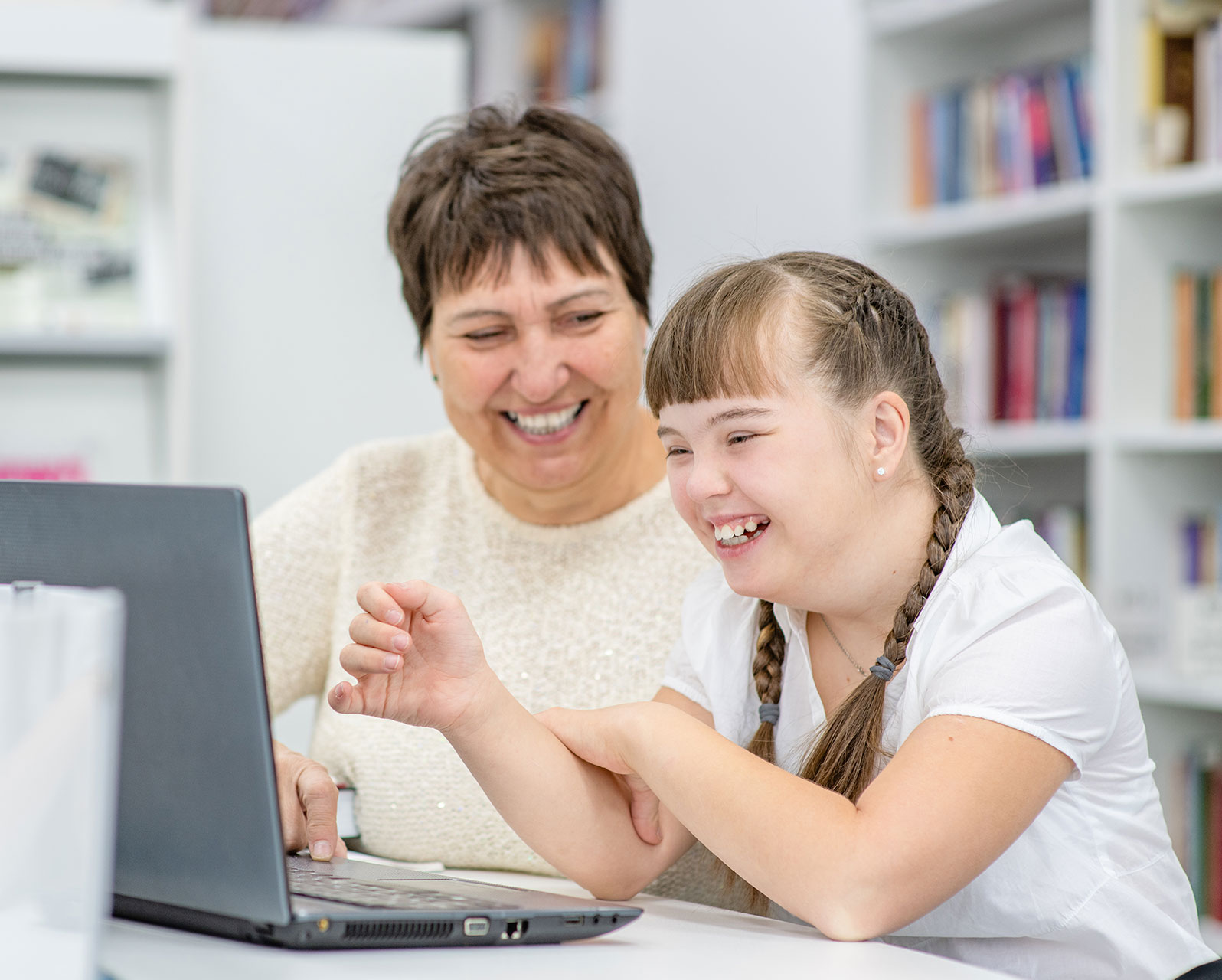 girl with down syndrome doing trainings or seeing a telehealth provider with her aid/mother beside her