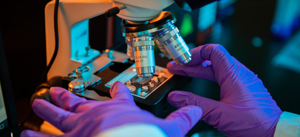 Ученый кладет предметное стекло под микроскоп