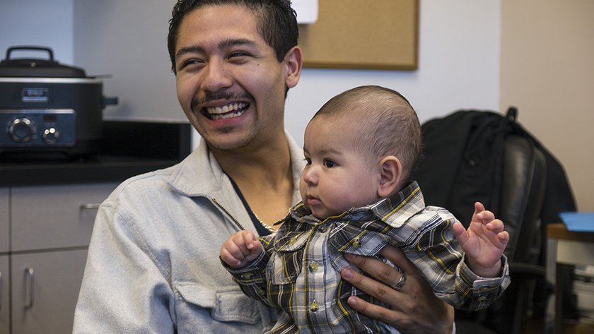 Um pai ri enquanto balança seu bebê sorridente no joelho