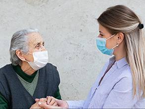 An elderly person with a caregiver, both wearing masks.