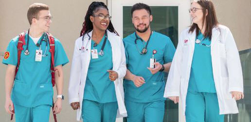 Four UNM medical students walk towards the camera in teal scrubs