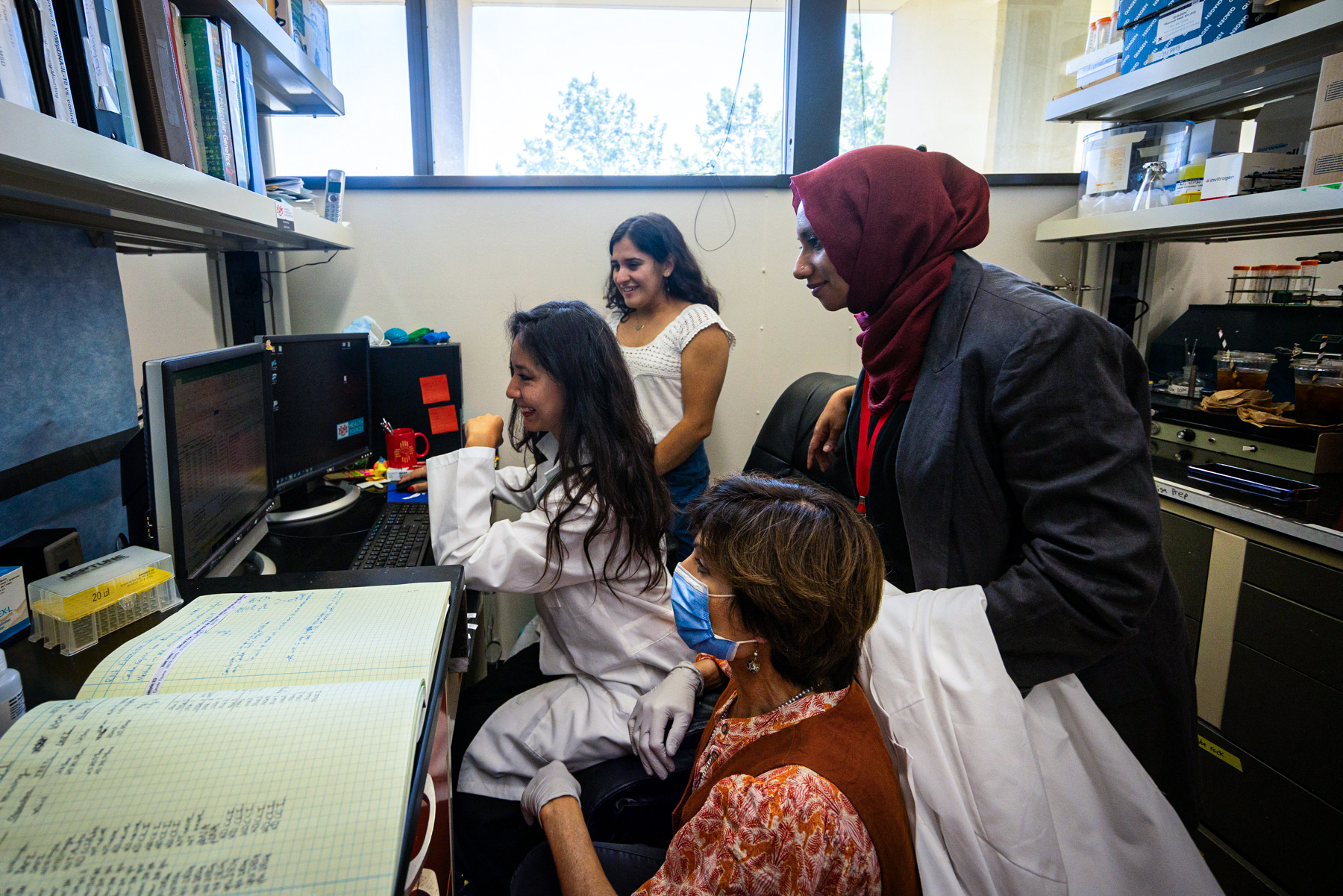 4 researchers are standing around a computer looking at results