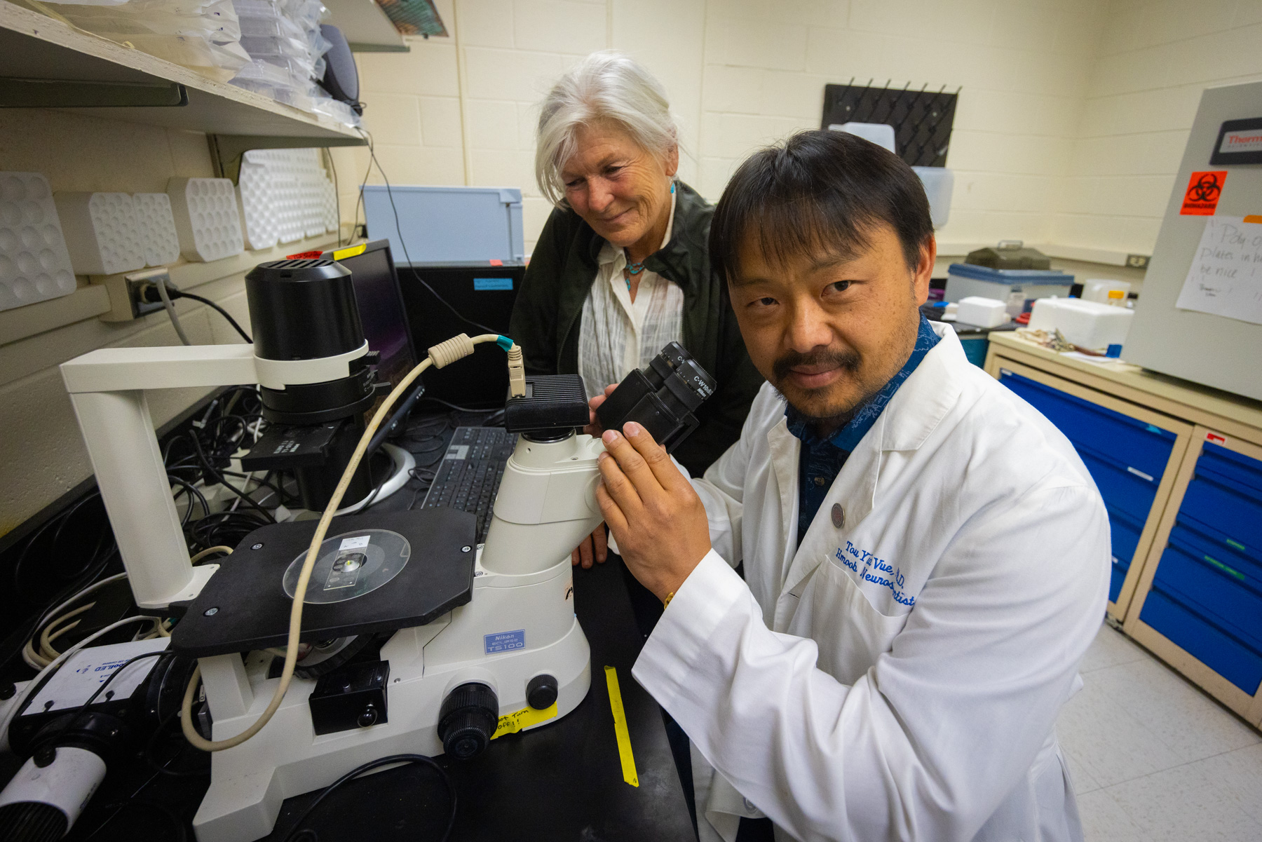 two researchers using a microscope to look at samples