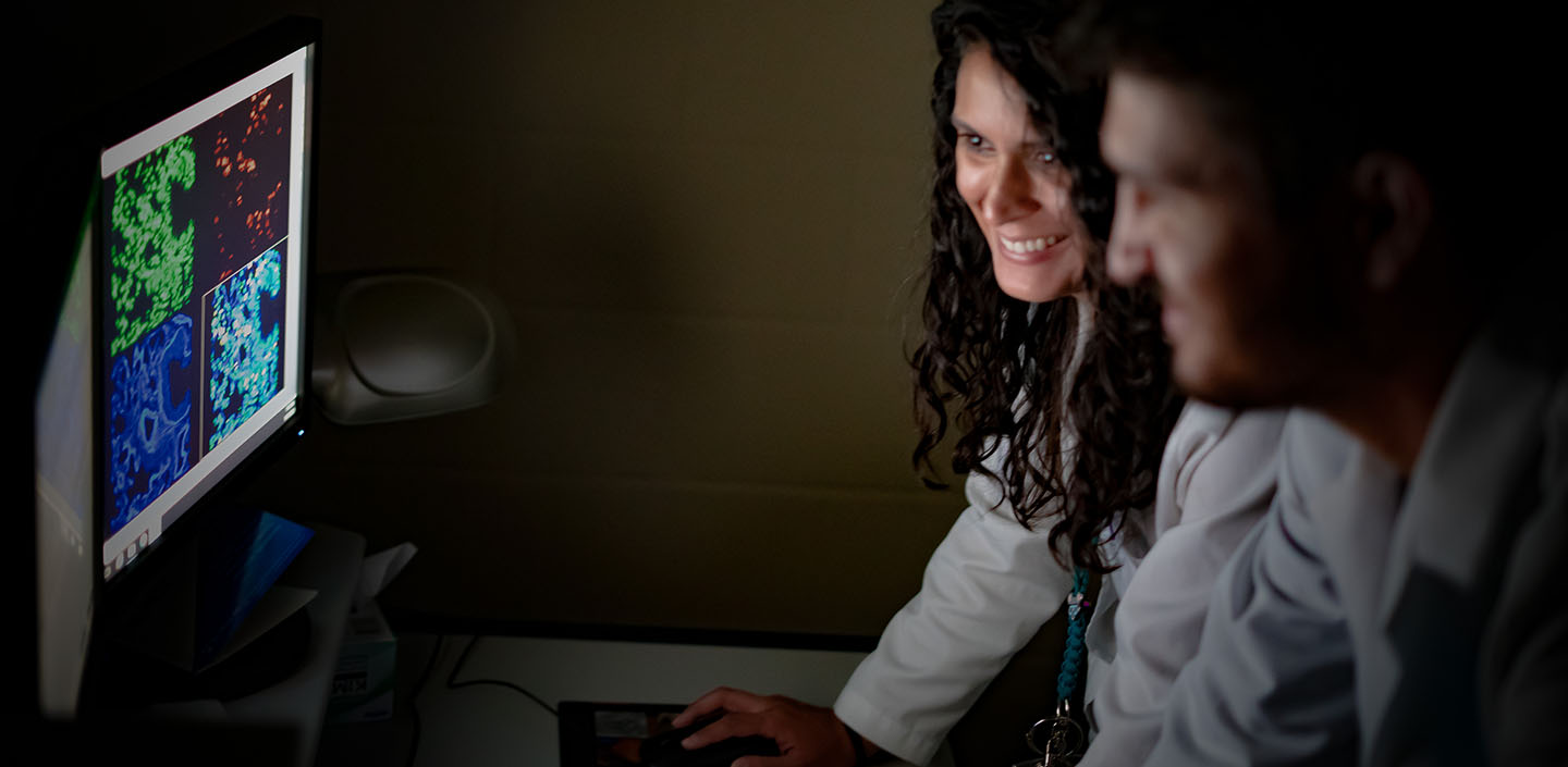 two researchers review data from a microscope at a computer