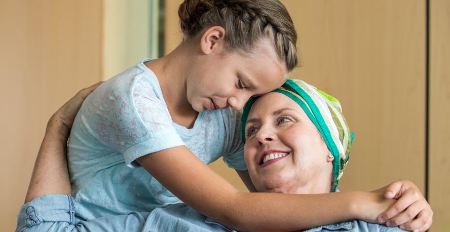 Una madre con cáncer abrazando a su hija, ambas felices y sonrientes