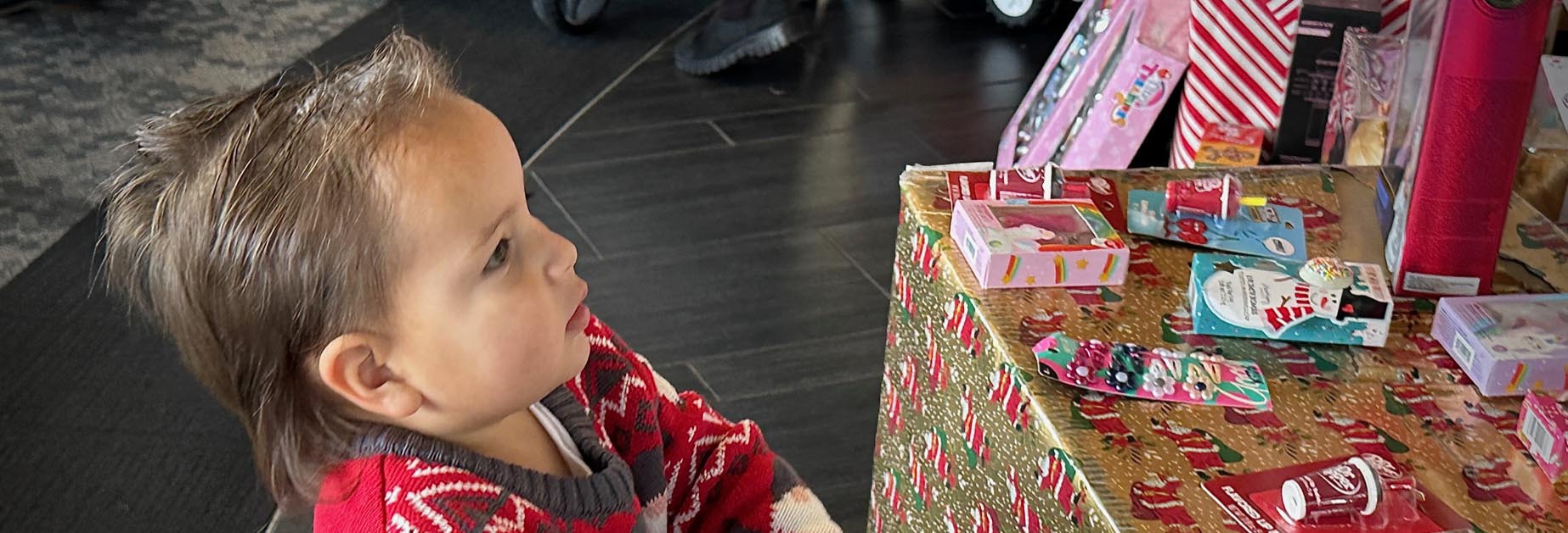 लपेटे हुए उपहारों के बगल में एक छोटा बच्चा
