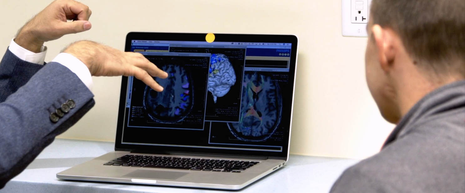 Zwei Personen betrachten einen Gehirnscan auf einem Laptop