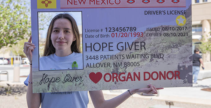 An organ donor posing with a novelty New Mexico ID that emphasizes being an organ donor