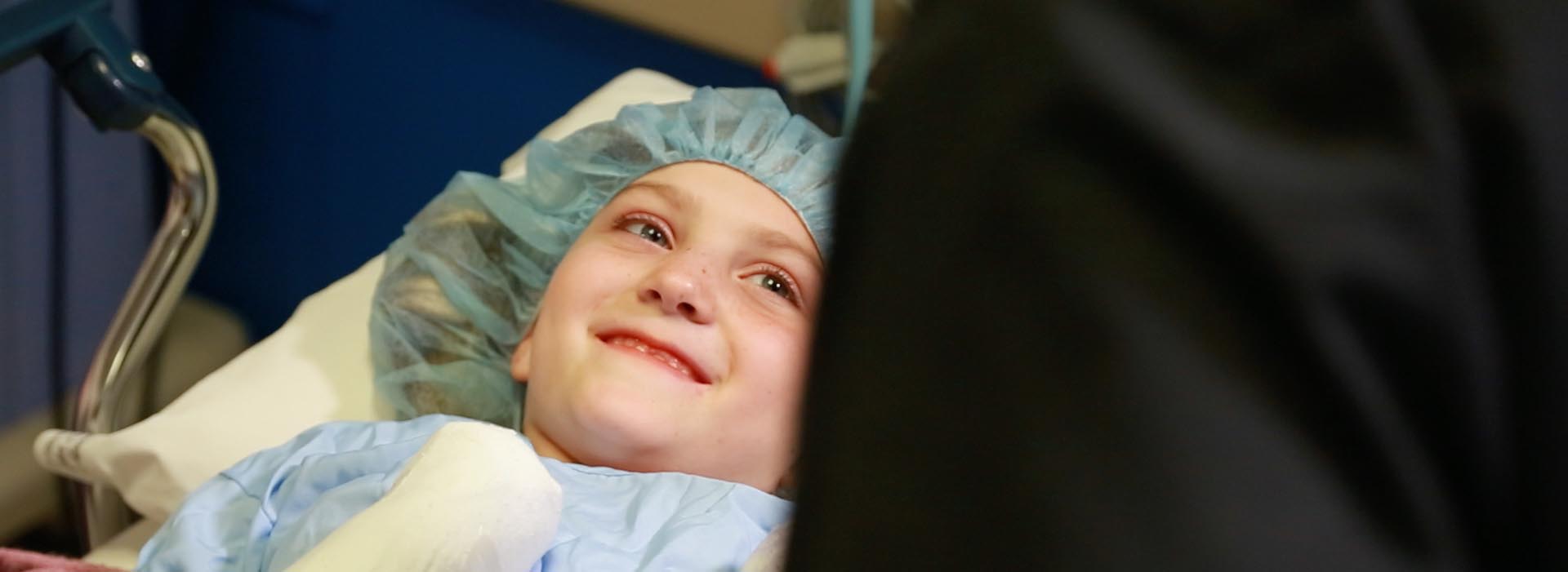 एक छोटा बच्चा मरीज फ्रेम से बाहर किसी को देखकर मुस्कुराता है