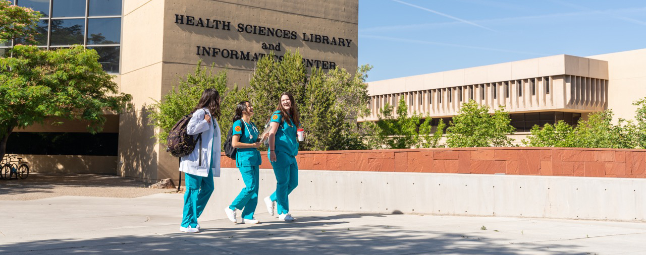 Three medical students walking in front of the Health Sciences Library building