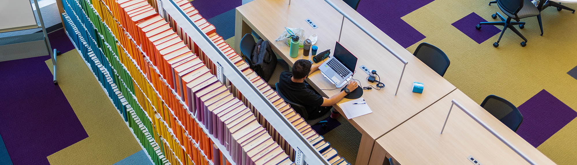 An birds eye view of a person studying in the HSC Library with a colorful array of books behind him
