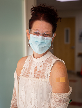 תמרה האו מחייכת כשהיא לובשת מסכה ומציגה בבנדייד היכן קיבלה חיסון נגד קוביד.
