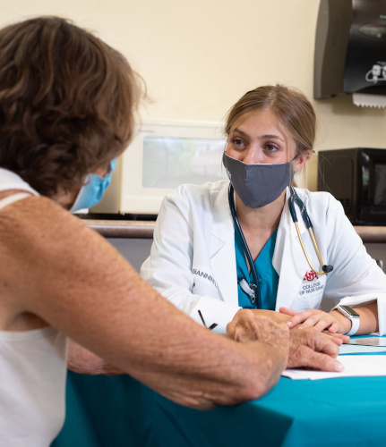 Étudiante en soins infirmiers parlant avec un patient à une table.