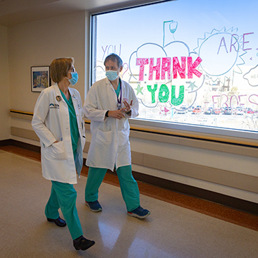 Jon Marinaro and Michelle Harkins walking by window decorated with the words Thank You.
