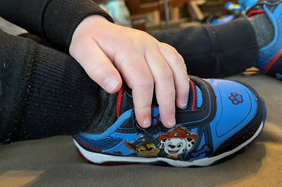 La mano del bambino piccolo sulle scarpe da pattuglia della zampa.